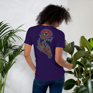 Woman wearing purple unisex t-shirt with psychedelic hand holding eye-flower design among green plants