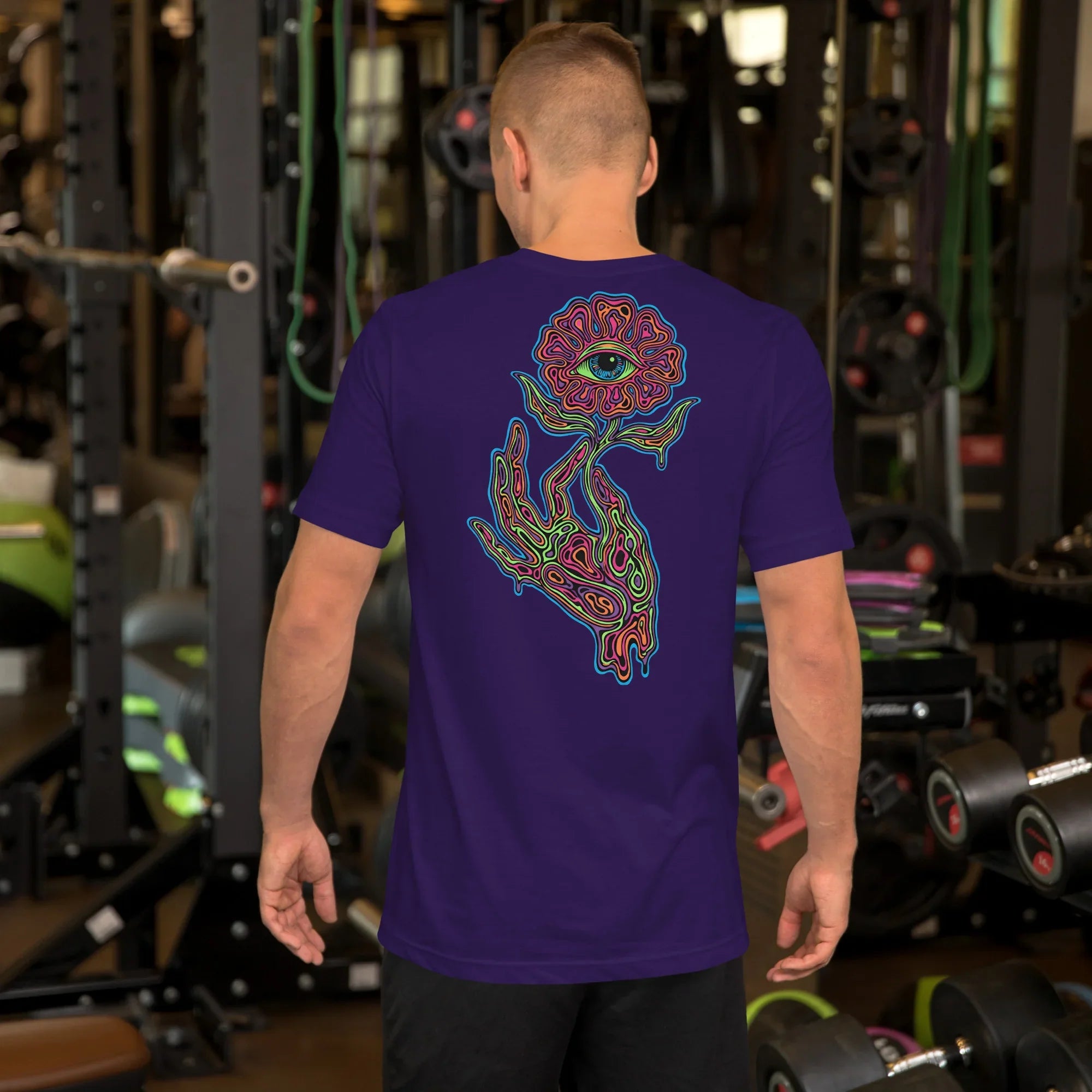 Man wearing unisex purple t-shirt with psychedelic hand and eye flower design in gym setting