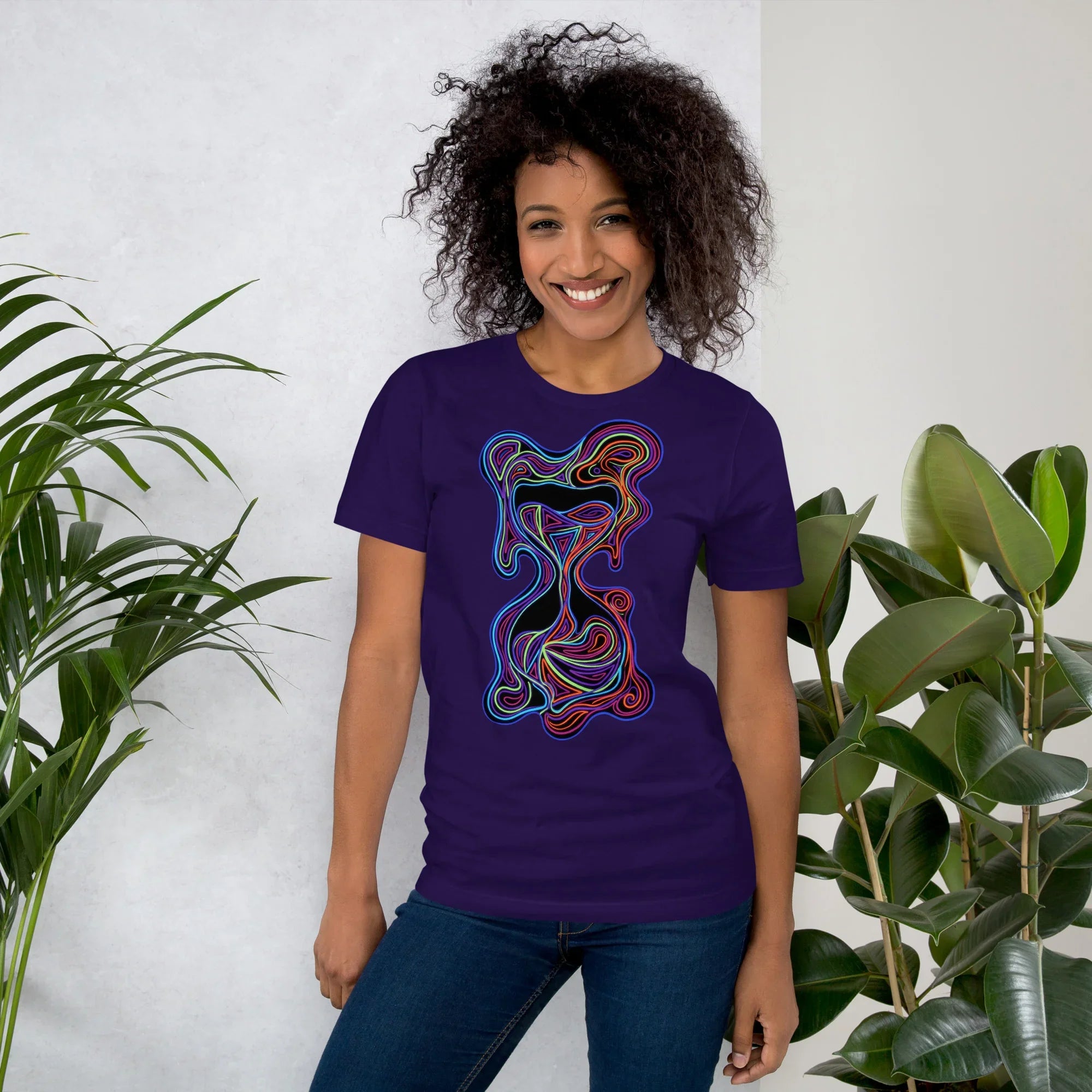 Smiling woman wearing a purple unisex staple t-shirt with abstract neon psychedelic art, standing between green plants