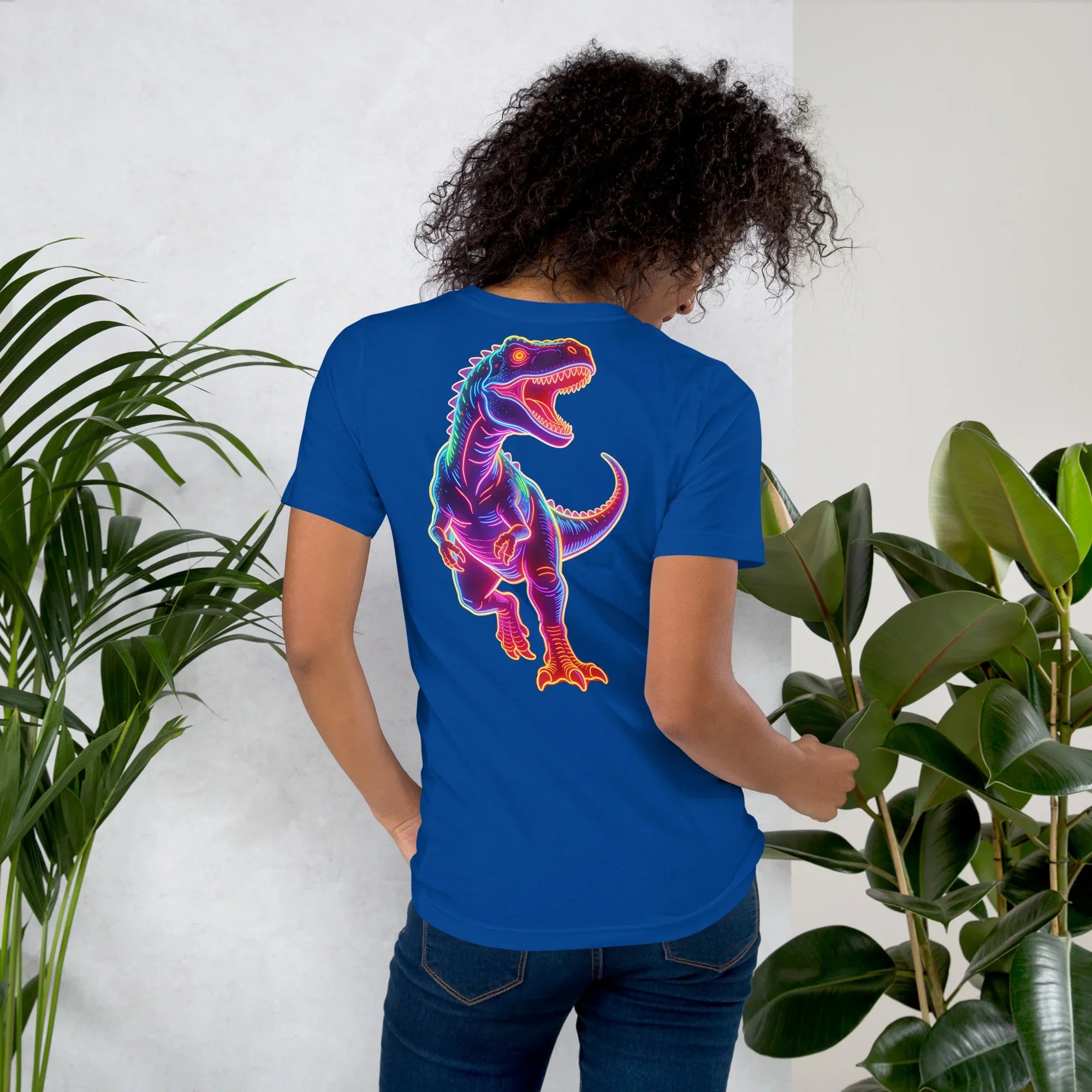 woman wearing true royal blue t-shirt with colorful neon roaring dinosaur graphic on back, indoor plant background