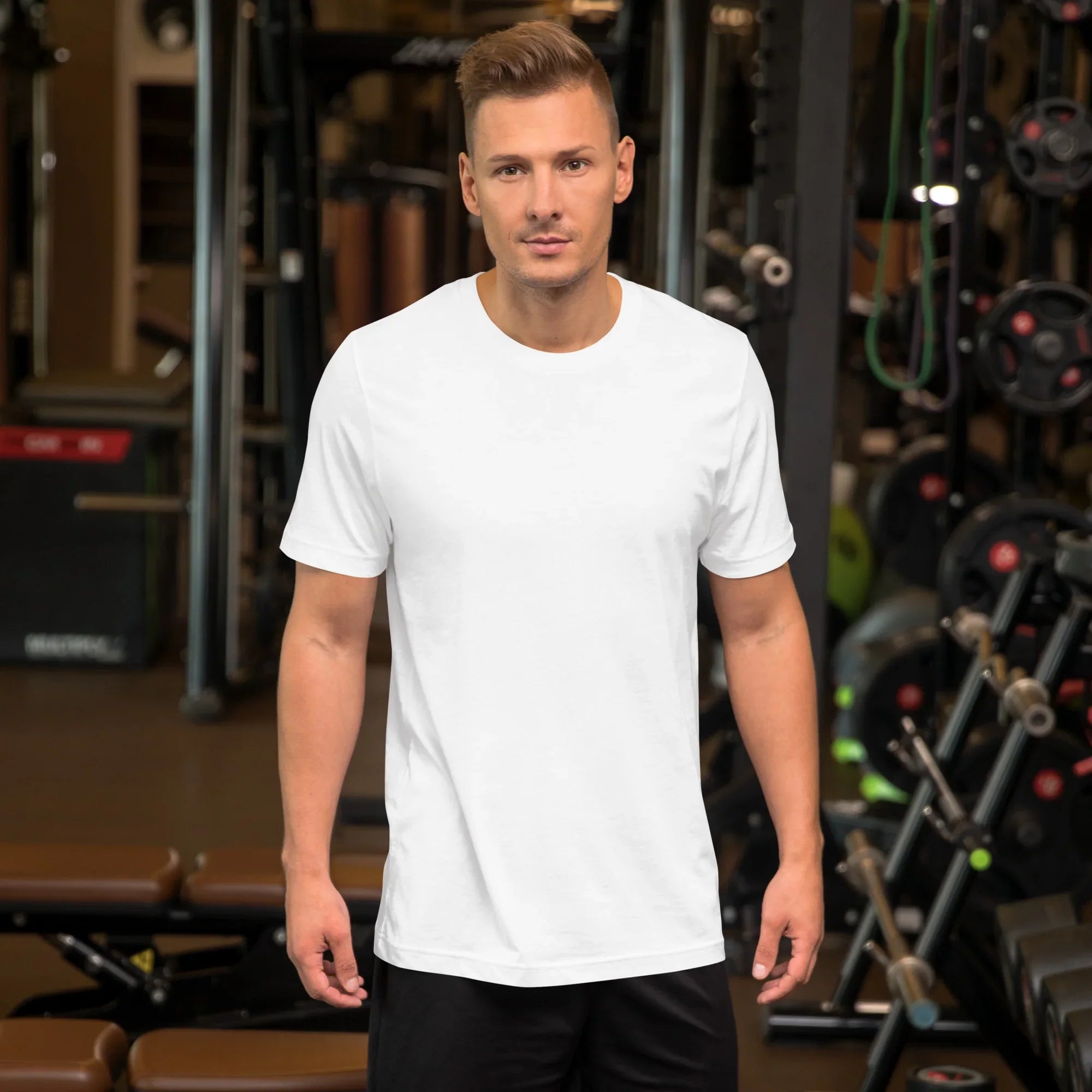 Man wearing a plain white unisex staple t-shirt in a gym setting with fitness equipment in background